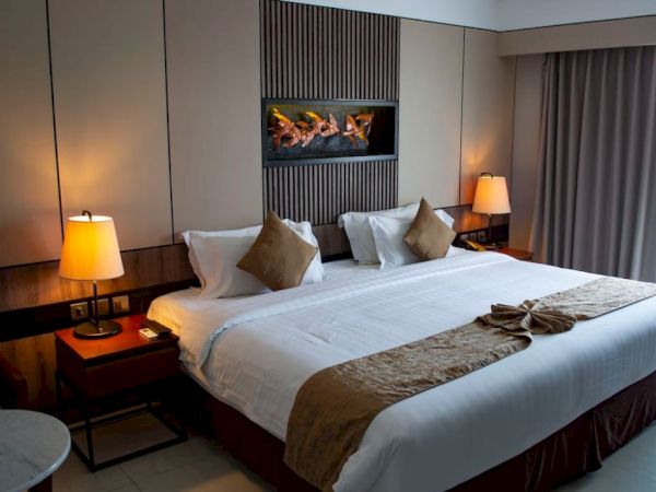 A modern hotel room features a large bed with pillows, bedside tables with lamps, a decorative wall piece, and a window with curtains.
