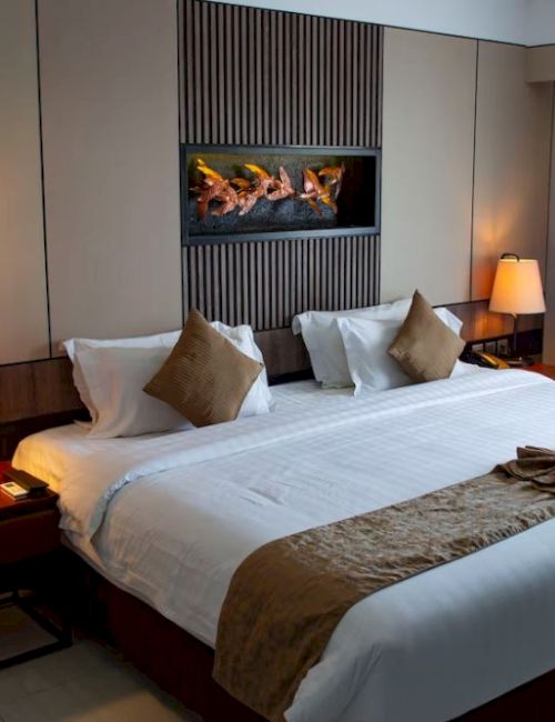 A modern hotel room with a neatly made bed, two lamps, decorative cushions, and wall art above the bed.