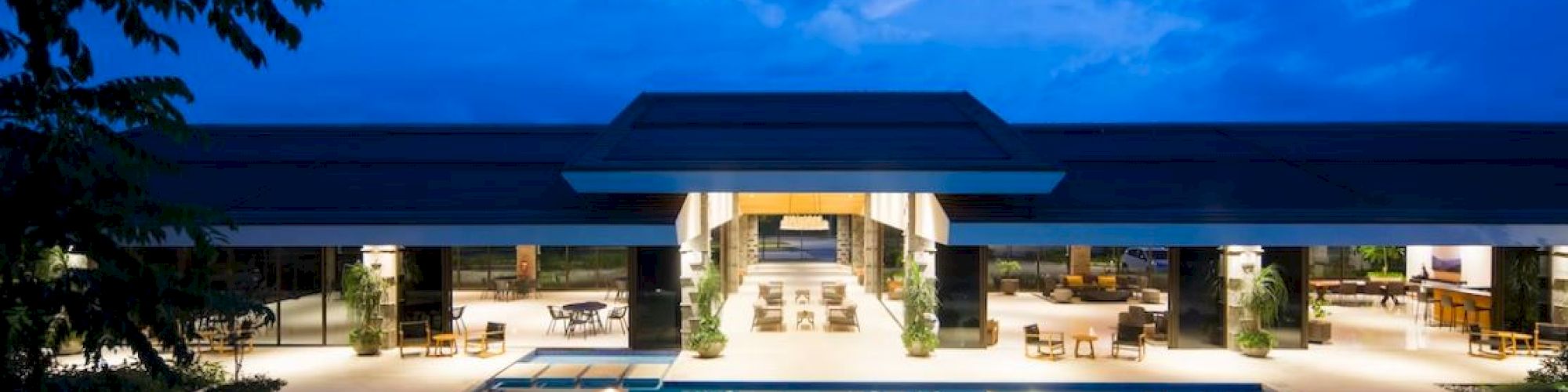 This image shows a luxurious outdoor pool area at night, with a modern building and bright interior lights reflecting on the water.