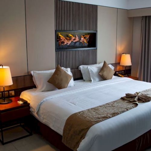 A hotel room with a neatly made king-size bed, two bedside lamps, and a wall decoration.