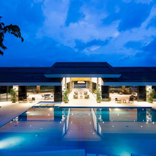 A luxurious pool area at night, with a modern building, ambient lighting, and seating arrangements.