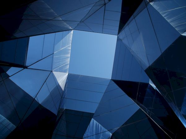 The image shows a geometric pattern of glass buildings with a blue sky visible in the center.