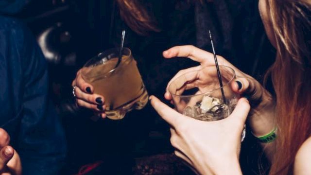 People are enjoying drinks and socializing in a lively setting, with smiles and dark attire visible.