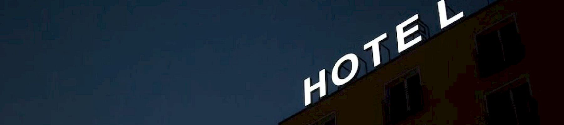 A building with the word "HOTEL" in illuminated letters on the roof, set against a dark evening sky.