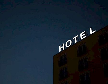 A building with the word "HOTEL" in illuminated letters on the roof, set against a dark evening sky.