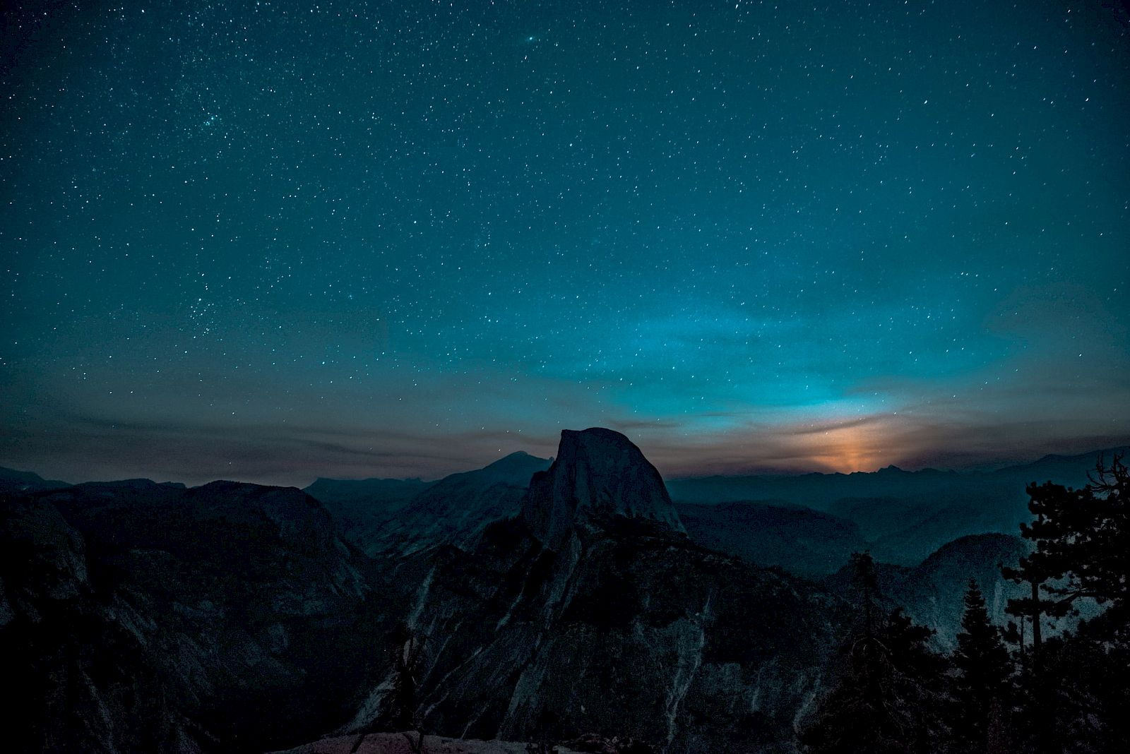 A starry night sky over a mountain landscape, with a soft glow on the horizon.