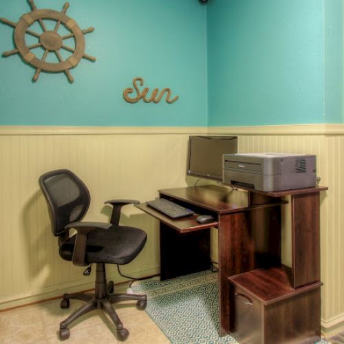A small office area with a computer, printer, and chair. Decor includes a helm and the word "Sun" on the wall.