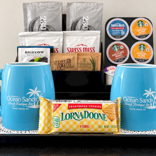 Two blue Ocean Sands mugs sit on a tray with coffee pods and Swiss Miss, plus Lorna Doone shortbread cookies.