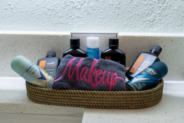The image shows a basket with toiletries, a towel labeled "Makeup," deodorants, and bottles, placed on a countertop.