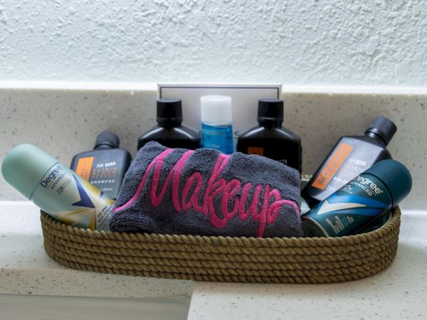 The image shows a basket with toiletries, a towel labeled "Makeup," deodorants, and bottles, placed on a countertop.