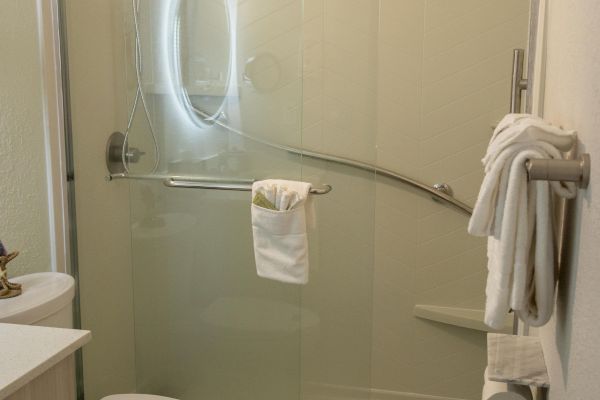 A modern bathroom with a shower, toilet, and sink. There are towels on racks and a sliding glass shower door.