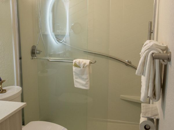 A modern bathroom with a shower, toilet, and sink. There are towels on racks and a sliding glass shower door.
