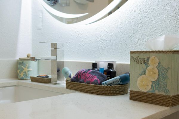 A bathroom countertop with a faucet, tissue box, and a basket of toiletries near a round mirror.