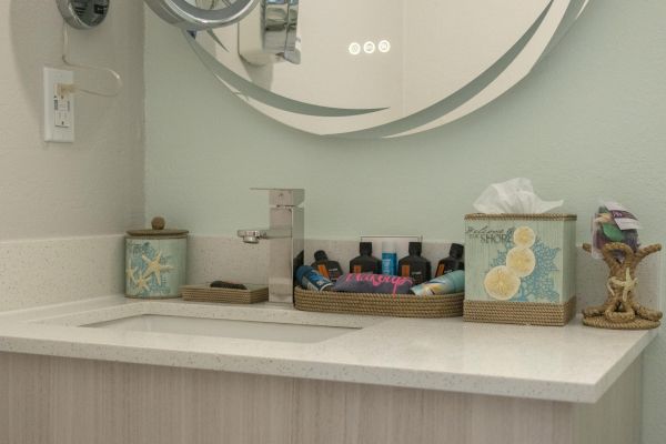 A bathroom sink with a modern faucet, a mirror, toiletries, a tissue box, and decorative items arranged on the countertop.