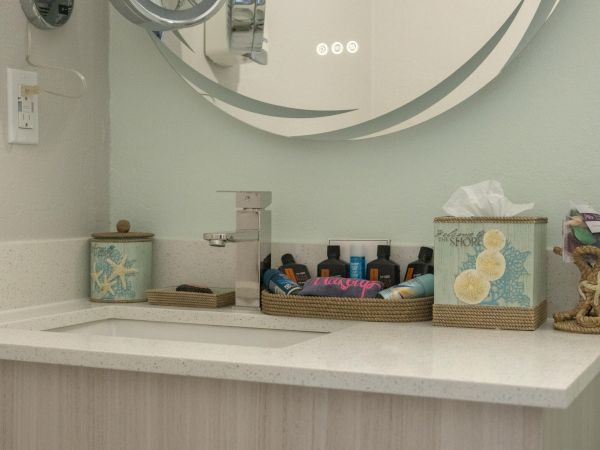 A bathroom sink with a modern faucet, a mirror, toiletries, a tissue box, and decorative items arranged on the countertop.