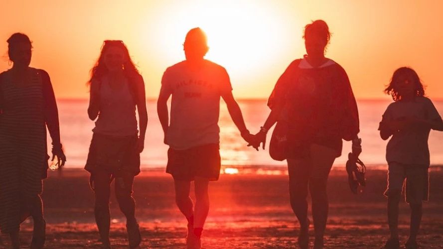 Silhouettes of five people walking hand in hand on a beach during a vibrant sunset over the ocean, creating a warm and serene atmosphere.