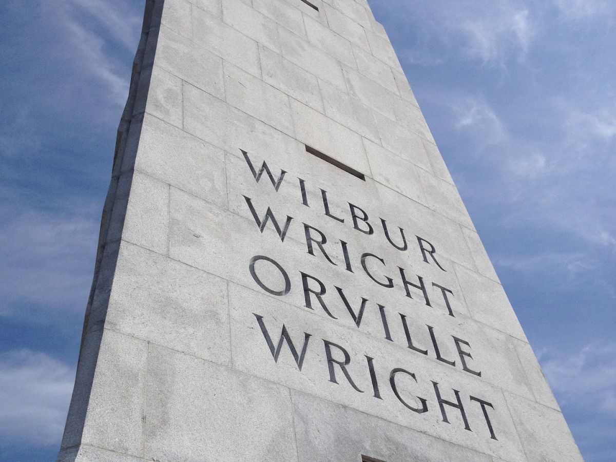 A tall stone monument with "Wilbur Wright" and "Orville Wright" engraved on it, set against a blue sky.