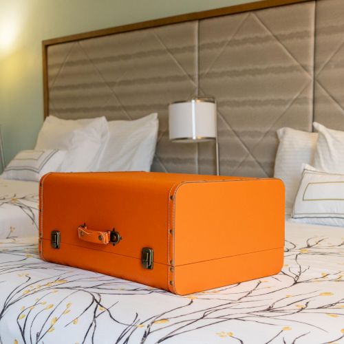 An orange suitcase sits on a bed with a patterned bedspread in a modern hotel room with two beds and stylish lighting.