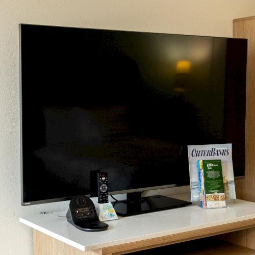 A TV on a stand with a remote, phone, and brochures.