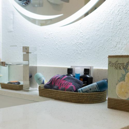 Bathroom countertop with a sink, soap dispenser, tissue box, and toiletries in a woven basket, under a round mirror.