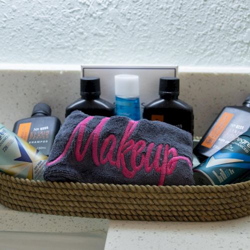 A basket contains toiletries, including deodorant, body wash, a small towel labeled "Makeup," and several bottles, on a countertop.
