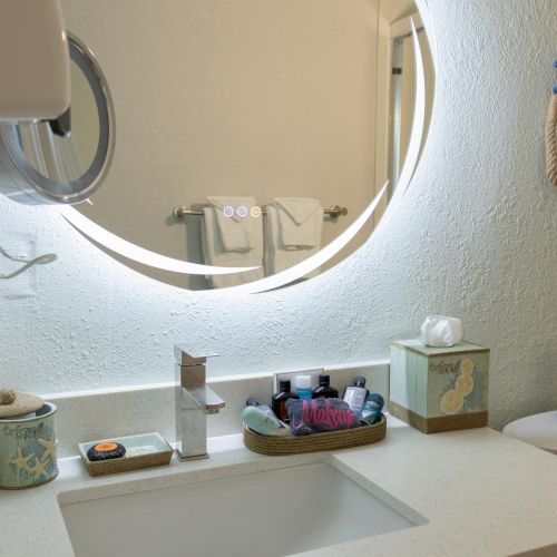 A bathroom sink with toiletries, a backlit mirror, soap, and tissues.