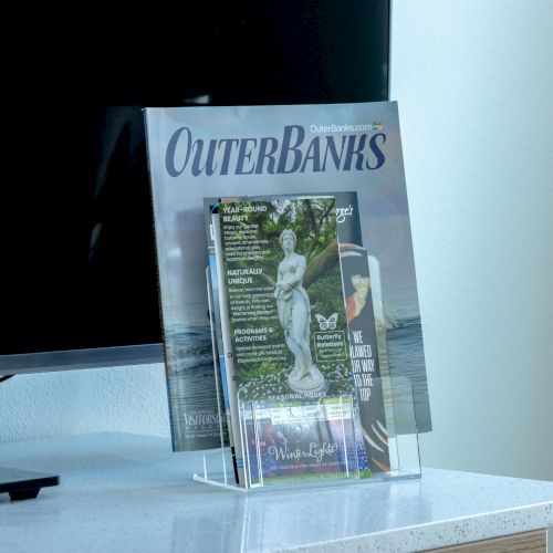 A magazine titled "Outer Banks" with brochures is displayed on a stand beside a TV on a countertop.