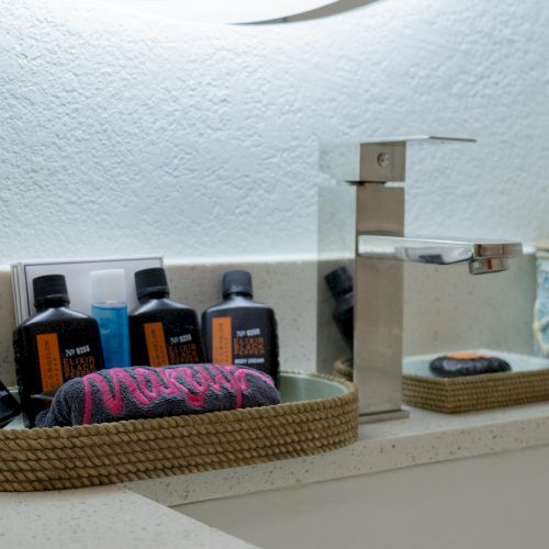 Bathroom counter with a modern faucet, toiletries in a woven basket, and a decorative jar with a starfish design.