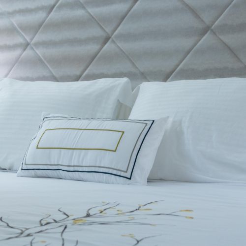 A neatly made bed with white pillows and a decorative pillow, alongside a nightstand lamp and a quilted headboard, creating a cozy atmosphere.