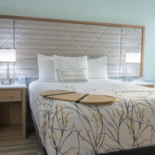 A modern bedroom with a neatly made bed, two bedside tables with lamps, and a decorative board on the bedspread.