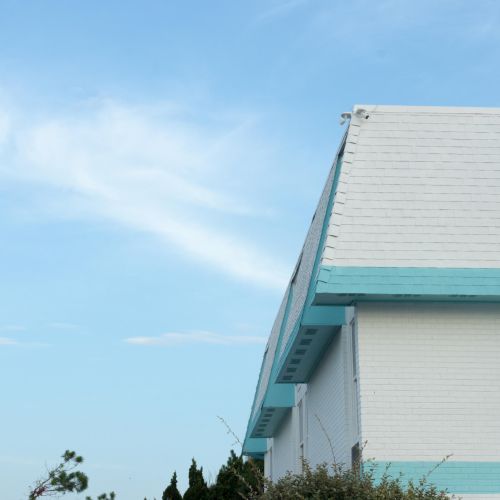 The image shows a building with a white and turquoise roof against a blue sky with the moon visible in the background.
