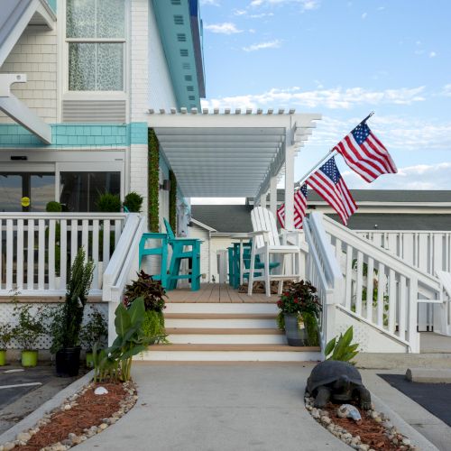 A house with a white pergola, patio furniture, American flags, and a landscaped walkway under a blue sky.
