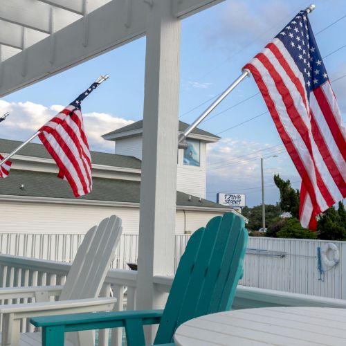 Outdoor seating area with American flags on display, featuring teal chairs and a white table.