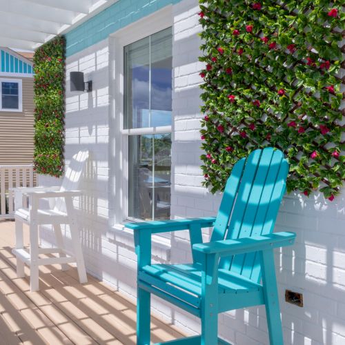 A porch with a turquoise chair, white siding, vertical greenery, and slatted overhead creating light and shadow patterns.