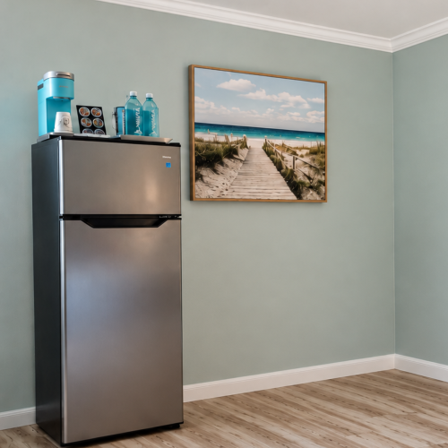 A stainless fridge with a water dispenser and bottled drinks on top, plus a framed beach walkway picture on the wall.
