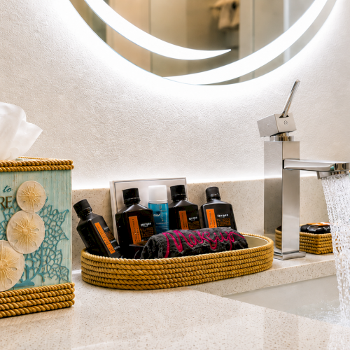 A bathroom vanity with a chrome faucet, soap bottles, tissue box, and beach-themed storage baskets, with water running.