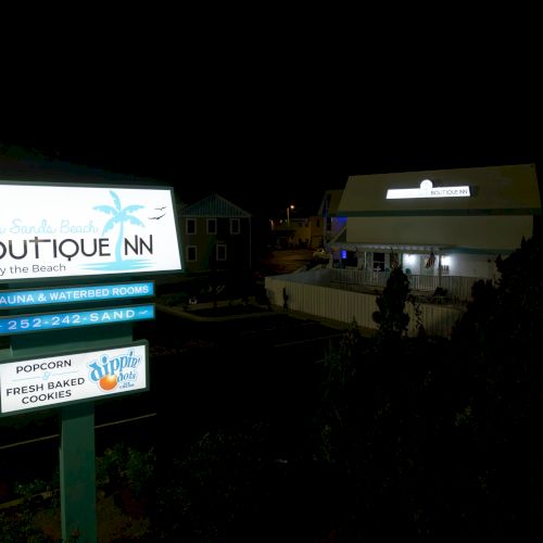 The image shows a sign for "Ocean Sands Beach Boutique Inn" by the beach, with features like a sauna and popcorn.