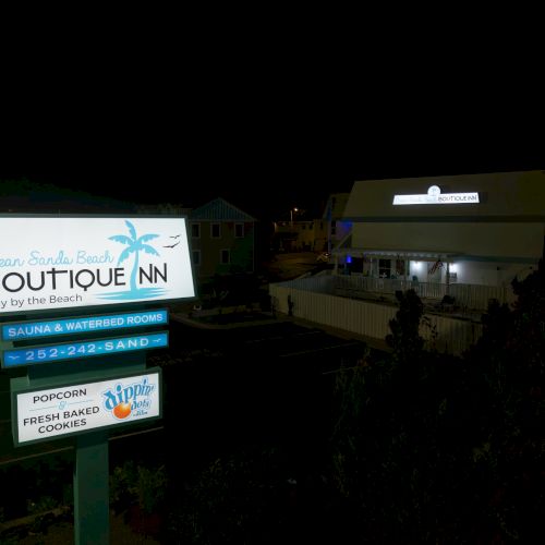 A small inn's signage at night reads "Ocean Sands Beach Boutique Inn" with amenities and contact details, set against a dark background.