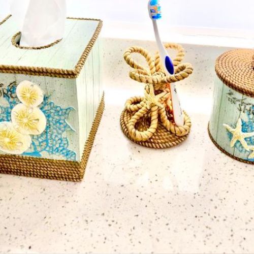 Bathroom countertop with beach-themed decor: a tissue box, toothbrush holder, and container with starfish and seashell designs.