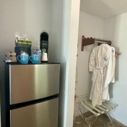 A kitchenette with a mini fridge, coffee maker, cups, and a robe on a rack in the corner.