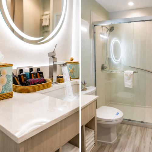 Bright hotel bathroom with a vanity, toiletries, and a glass shower with towels and a glowing mirror.