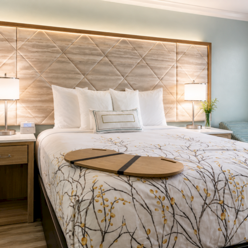 A stylish hotel bedroom with a neatly made bed, decorative headboard, bedside lamps, and a window with curtains.