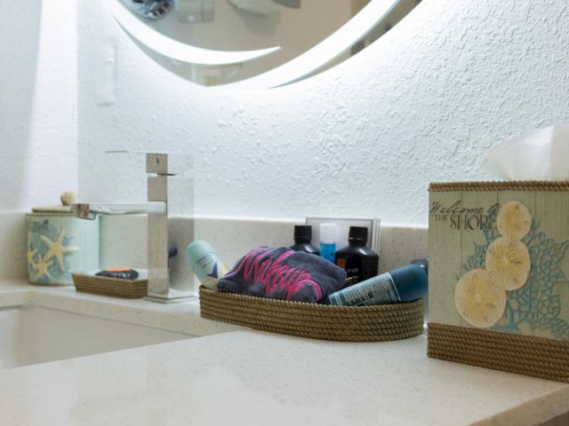 A bathroom countertop with a faucet, tissue box, and trays holding toiletries under a round mirror against a white wall.