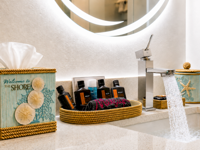 A bright bathroom counter with wicker bins of towels, soap bottles, starfish decor, and a sink faucet with running water.