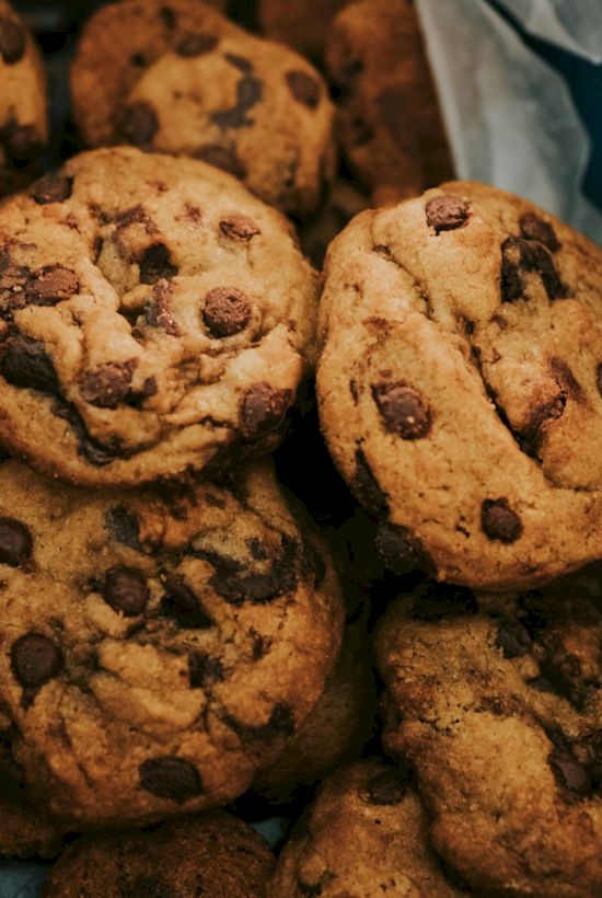 A box of homemade chocolate-chip cookies with melted chips, including one cookie shaped like a face.