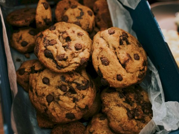 A box of chocolate chip cookies, some with spooky faces, fresh and golden with dark chips peeking through.