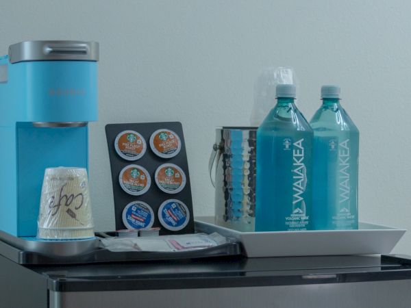 A Keurig coffee pod and accessories station with decaf pods and two bottles of Waiakea bottled water on a tray.