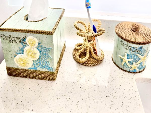 Decorative beach-themed toothbrush and woven holders with shell artwork on containers and a blue-and-white shell theme.