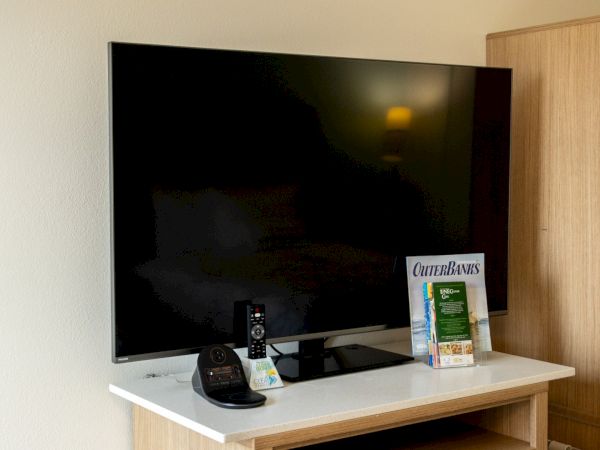 Flat-screen TV on a wooden media stand with a remote and cookbooks on the shelf.