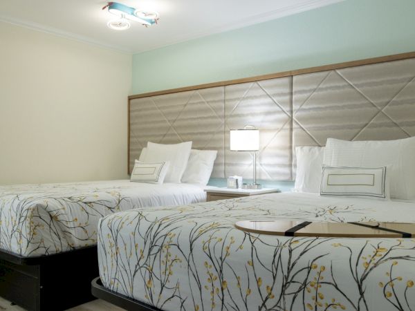 A modern twin bedroom with two beds, patterned white-and-gold bedding, upholstered headboard, and bedside lamps.